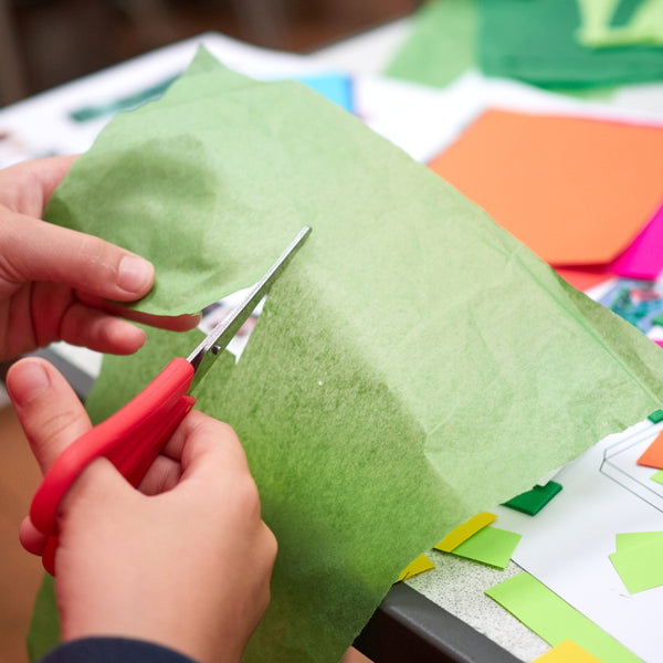 Person cutting green paper with red scissors on a colorful background